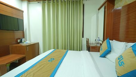 Side view of a deluxe room featuring a king size bed, a television, and a window covered by curtains at DLS Hotels The Rock Castle.